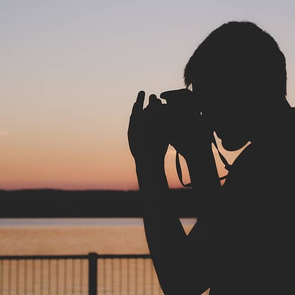 Silhouette d'un homme en train de prendre une photo du soleil qui se couche