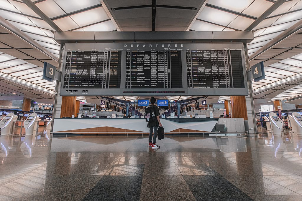 Un voyageur dans un aéroport devant un grand tableau d'affichage des vols
