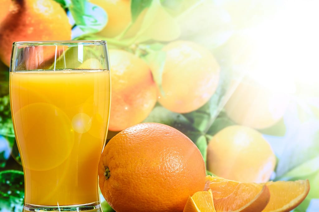 verre de jus d'orange au soleil entouré d'oranges entières