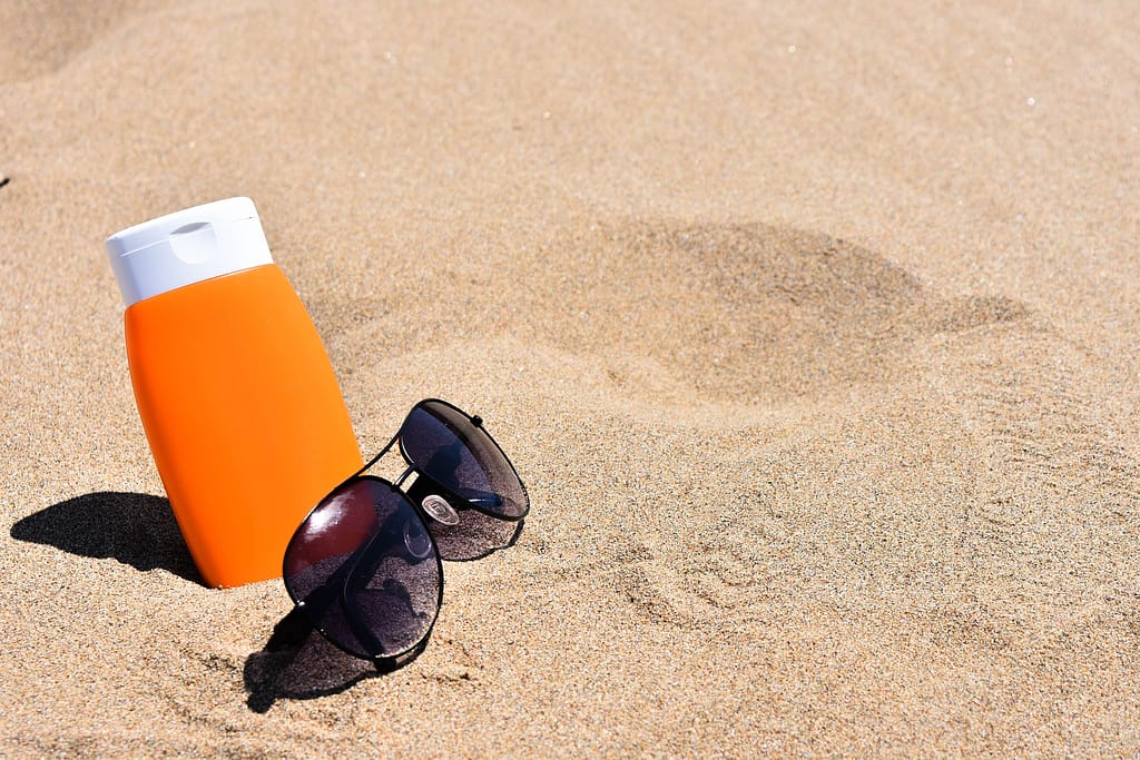 tube de crème solaire planté dans le sable à côté de lunettes de soleil