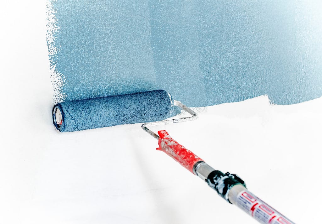 rouleau de peinture bleu utilisé pour peindre sur un mur blanc