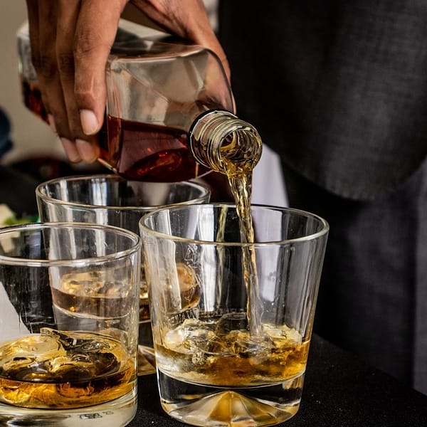 personne qui sert trois verres de whisky