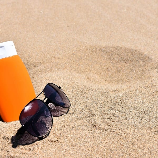 tube de crème solaire planté dans le sable à côté de lunettes de soleil