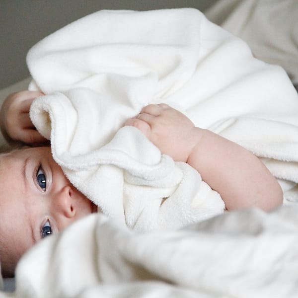 bébé sous des draps qui regarde l'objectif de l'appareil