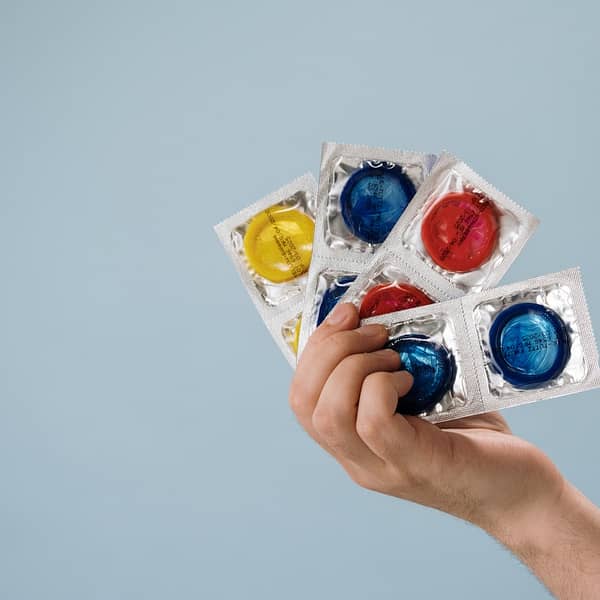 plusieurs préservatifs de différentes couleurs dans une main
